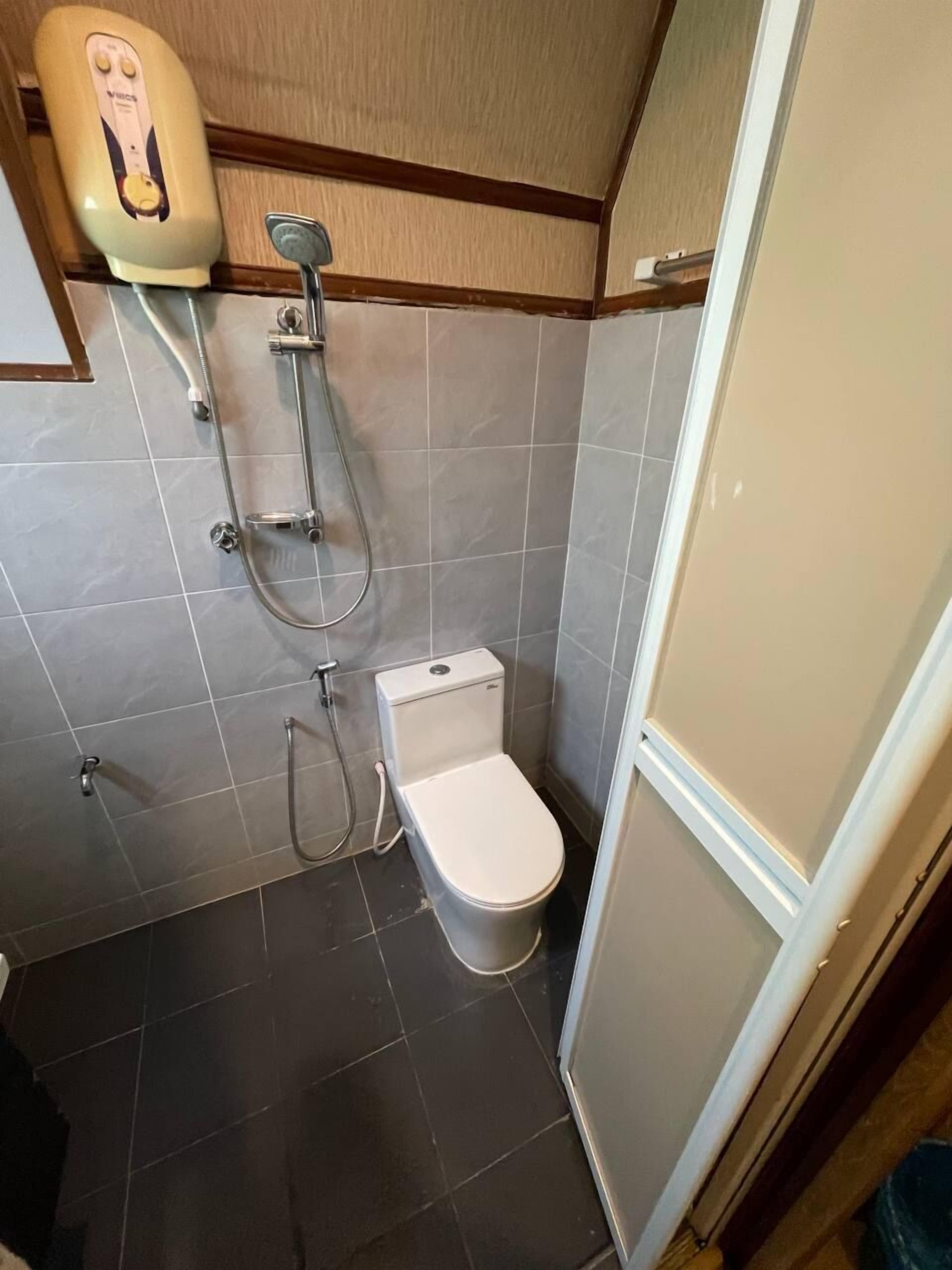 A compact bathroom with a toilet, a shower unit, and a hand dryer.