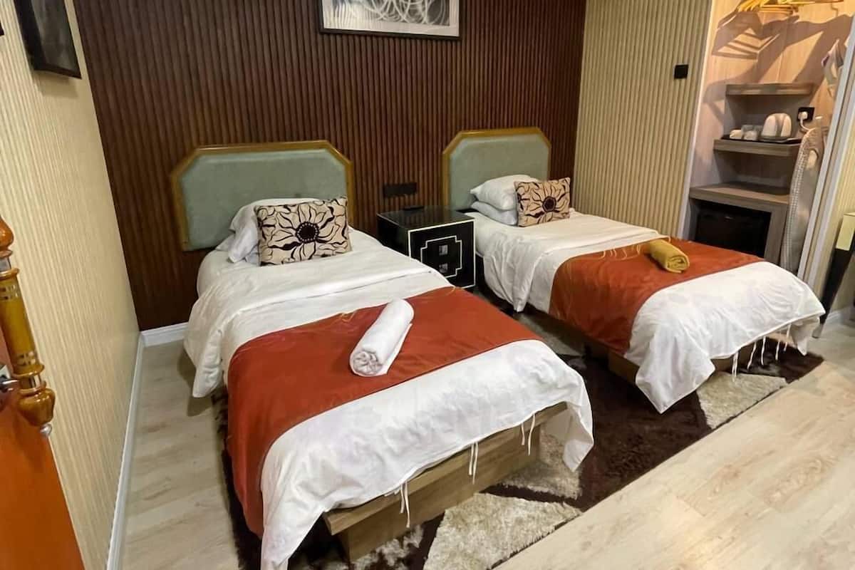 Quarto de hotel com duas camas, ventilador de teto, aparelho de ar condicionado e guarda-roupa com roupas penduradas.