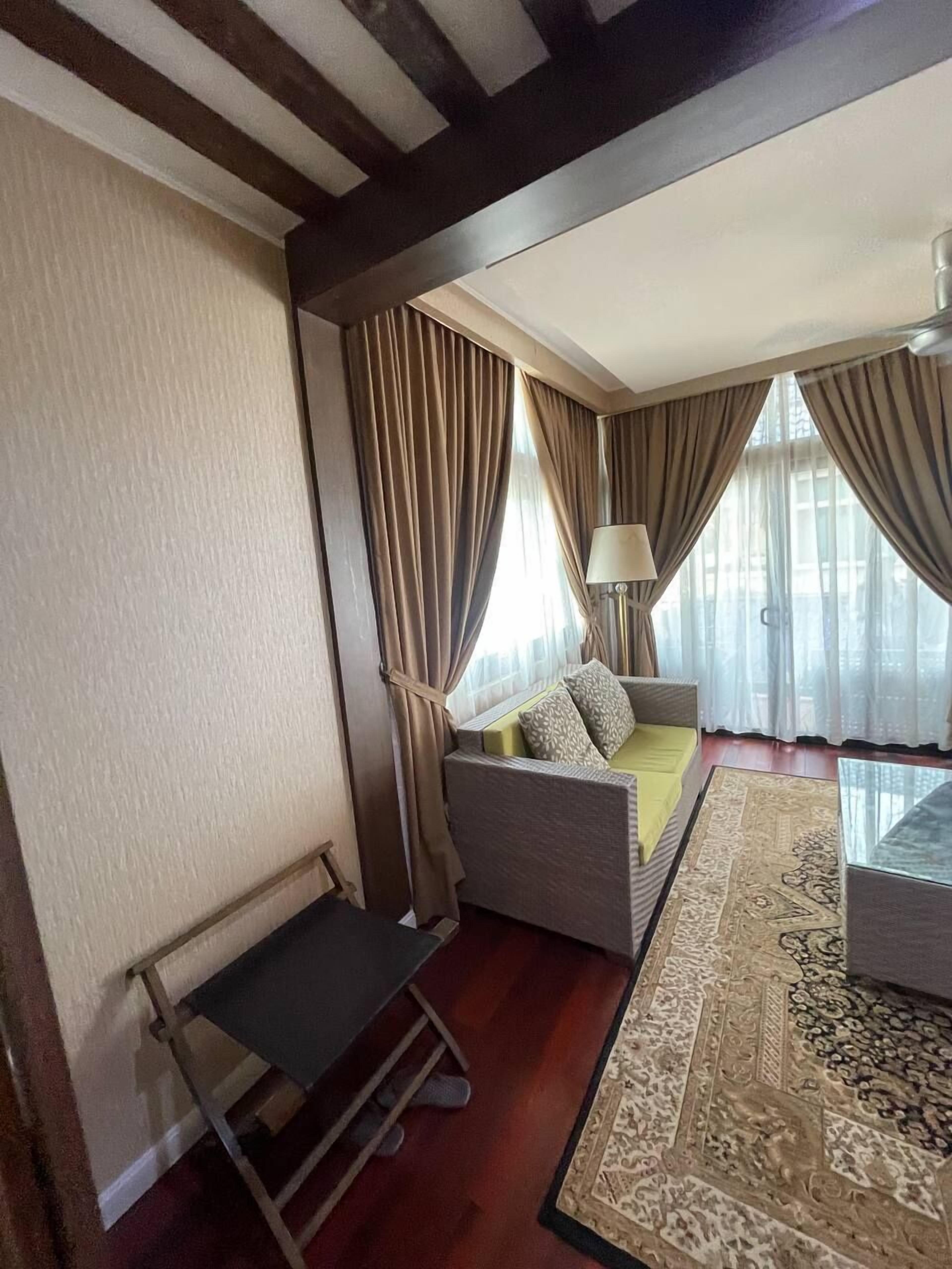 A hotel room with a sofa bed, a small table, a lamp, and a patterned rug.