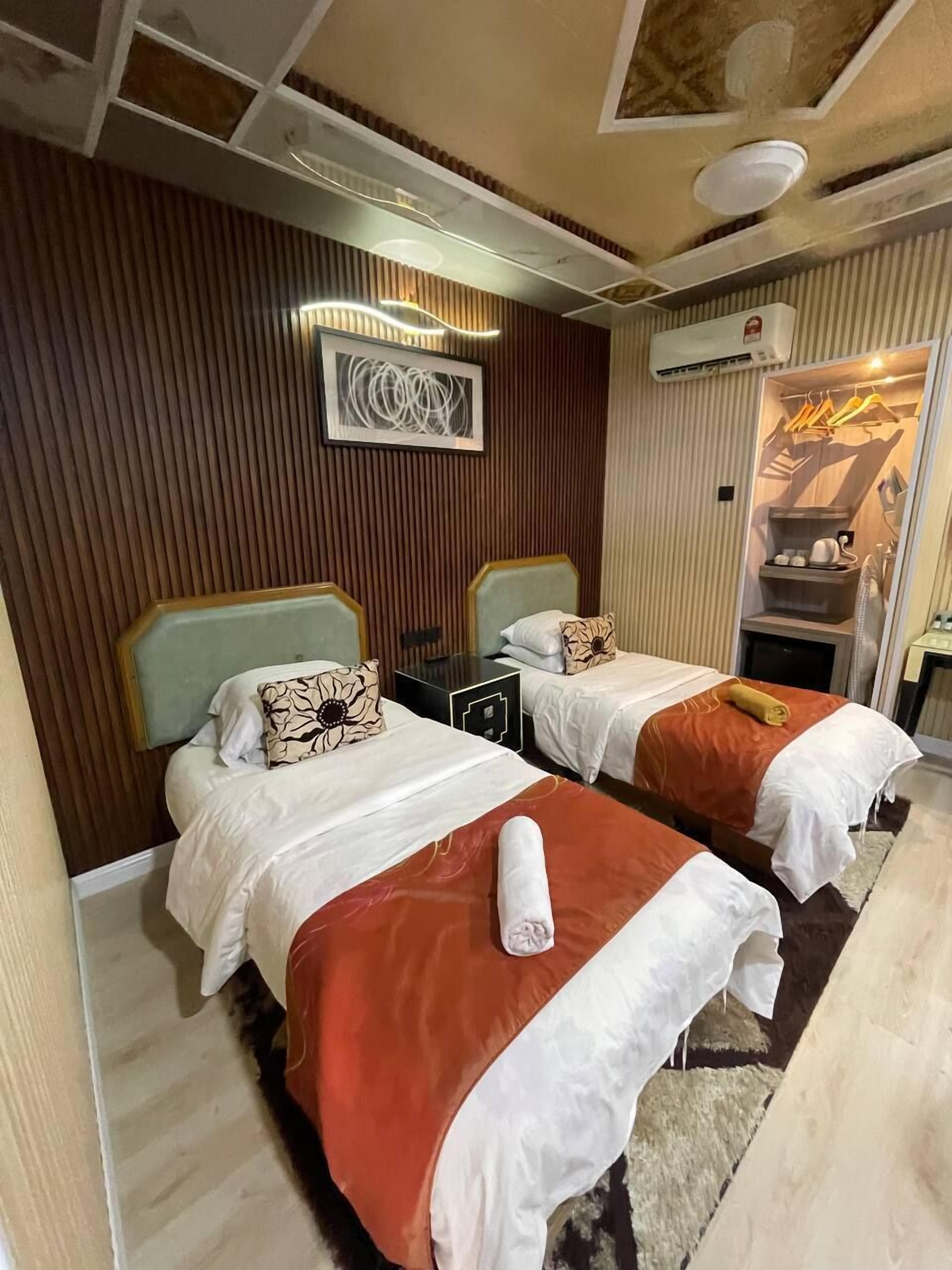 A hotel room with two beds, a wooden panel wall, a ceiling light, and an air conditioning unit.