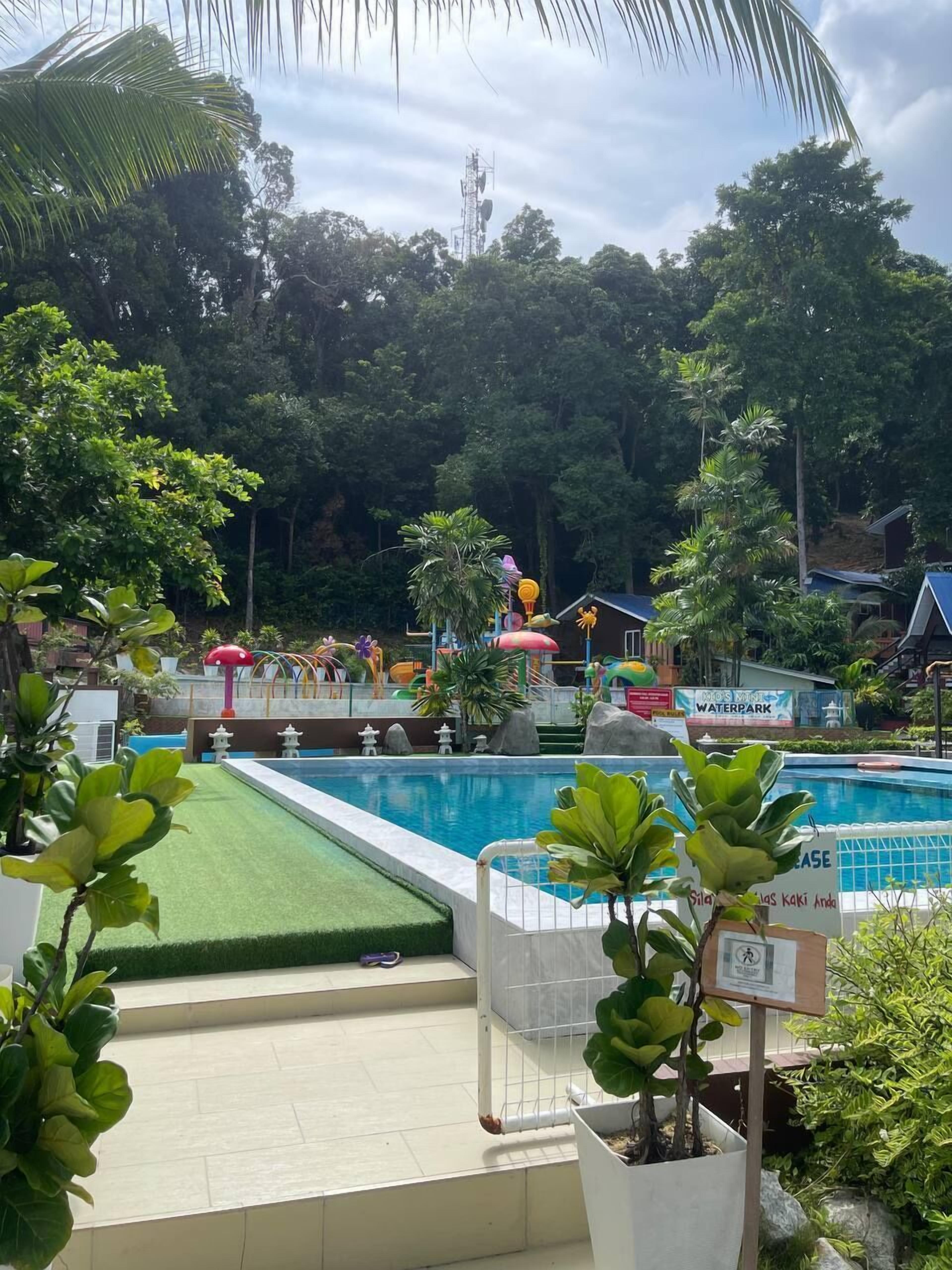 Een zwembad met een bord voor een waterpark, omringd door weelderige begroeiing en palmbomen.