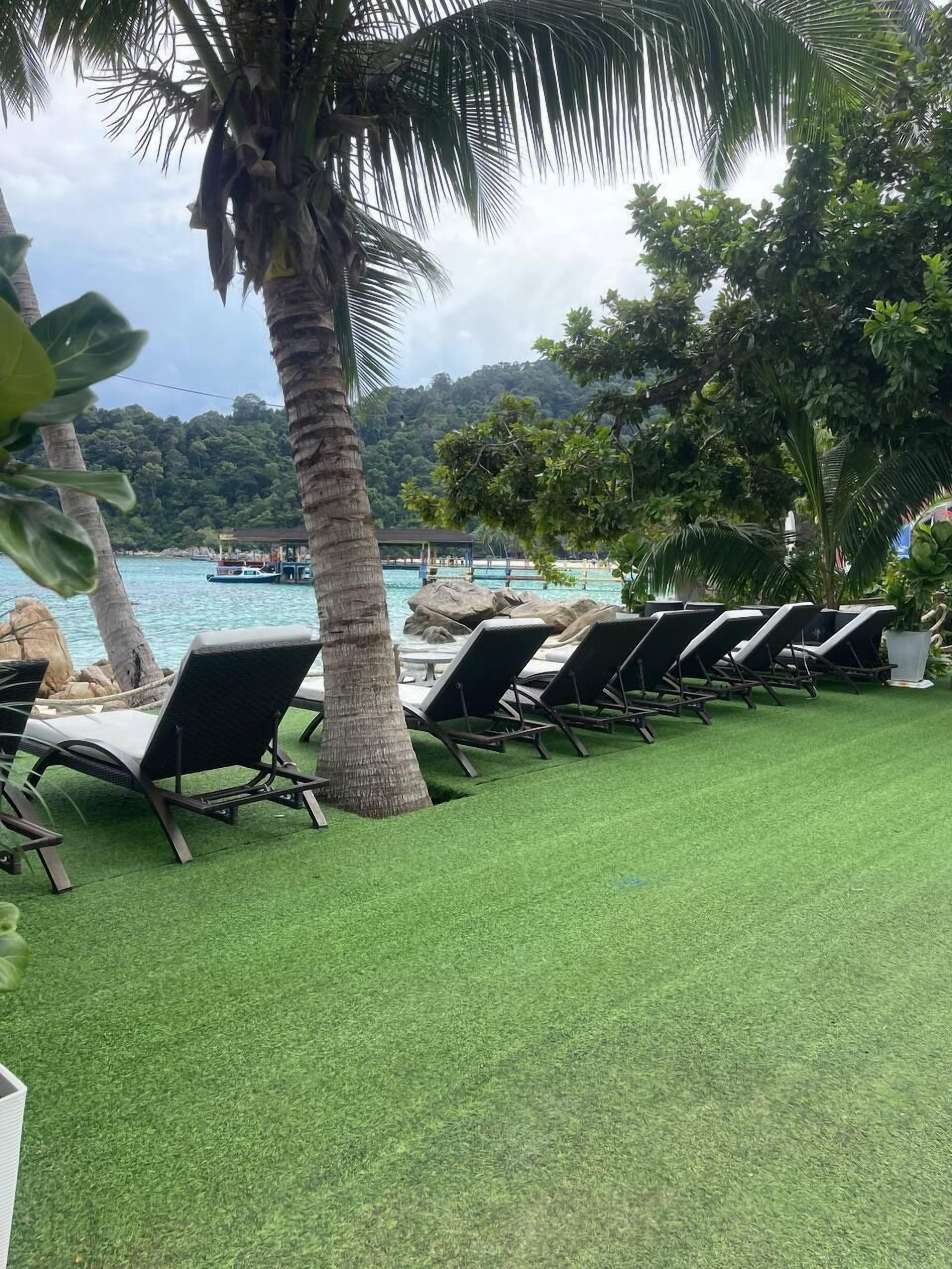 A row of sun loungers on a green lawn with a view of a body of water and a boat in the distance.