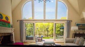 A spacious living room with a high ceiling, large windows, and a chandelier. - Sensational & Sophisticated 5 Bedroom Home in East Hampton (East Hampton)