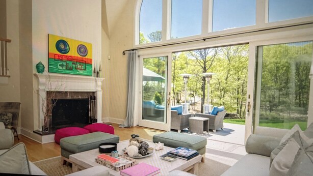 A spacious living room with a fireplace, large windows, and outdoor seating area. - Sensational & Sophisticated 5 Bedroom Home in East Hampton (East Hampton)