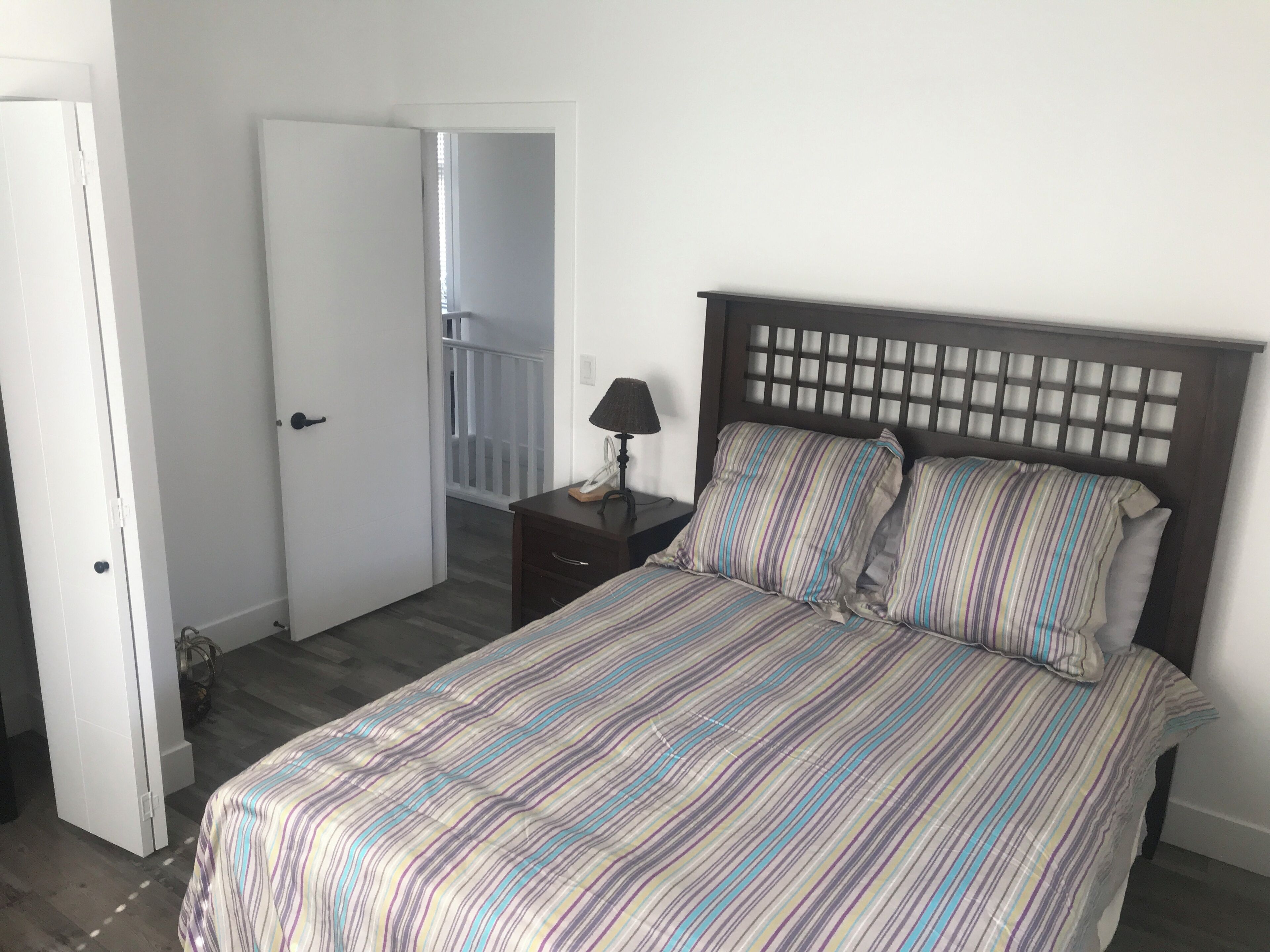 A bedroom with a bed, a nightstand, a lamp, and a door leading to a balcony.