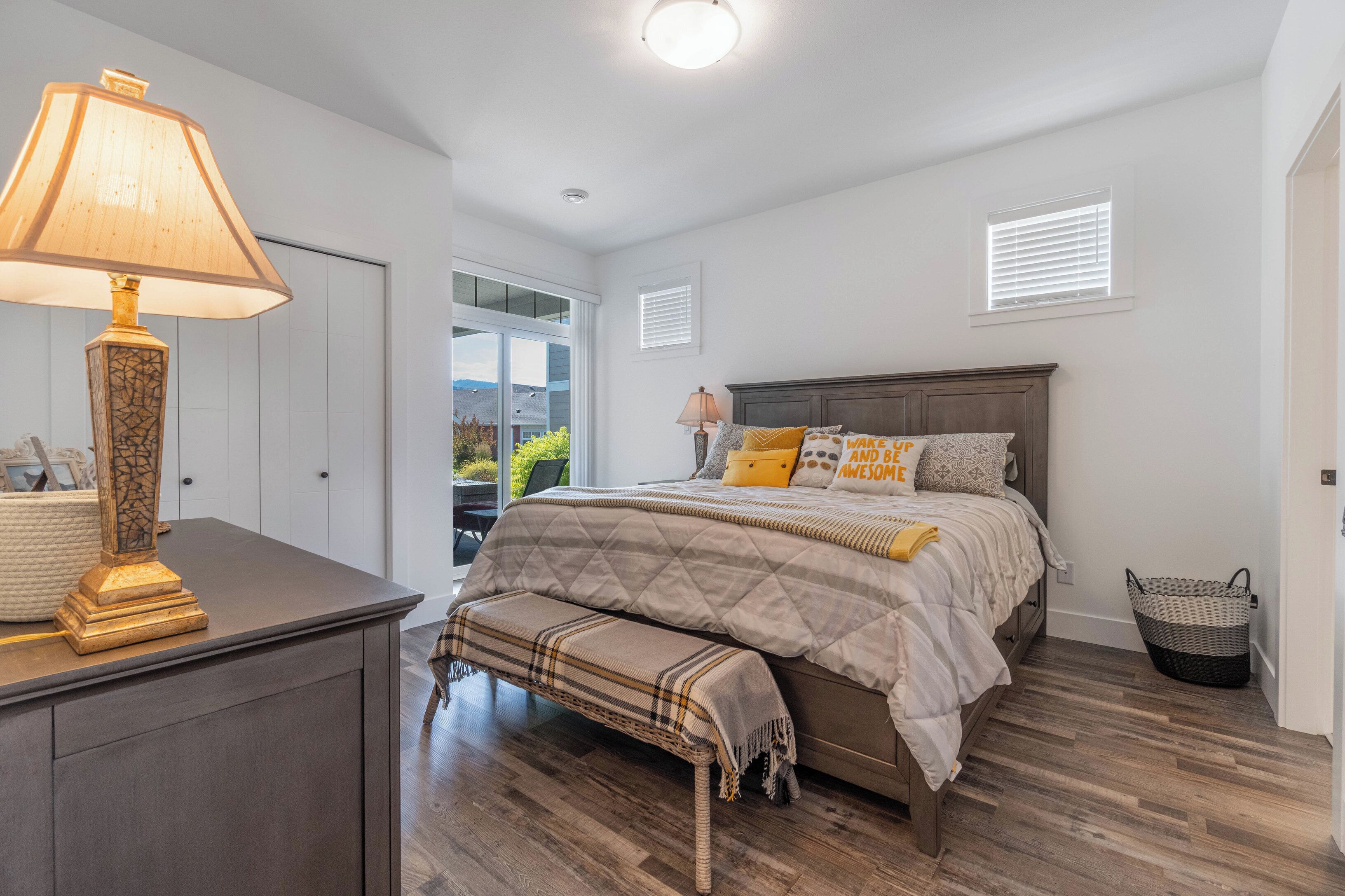 A bedroom with a bed, bedside lamp, bench, and a window with blinds.
