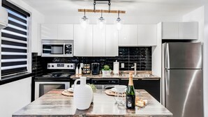 Eine moderne Küche mit weißen Schränken, Edelstahlgeräten und einer Holztheke, auf der eine Champagnerflasche und Gläser stehen.
