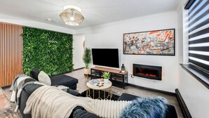 Ein modernes Wohnzimmer mit Flachbildfernseher, Kamin, einer grünen Wand und einer Couch mit Überwurfdecke.