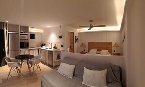 A modern hotel room with a kitchenette, a dining area, and a large bed.