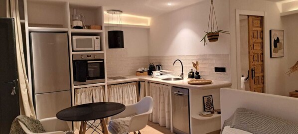A compact kitchen with a refrigerator, microwave, oven, and sink. There's a dining area with a table and chairs, and a sofa in the living space.