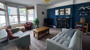 A living room with a fireplace, a television, and a bookshelf. - Seaside Apartments (Ilfracombe)