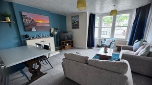 A living room with a dining area, a sofa, a TV, and a fireplace. - Seaside Apartments (Ilfracombe)