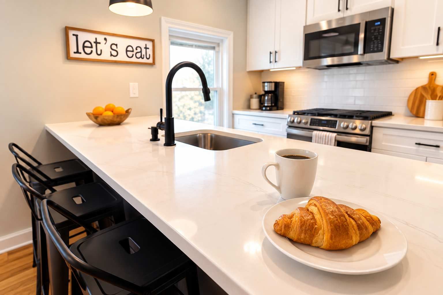 A modern kitchen with a white countertop, black bar stools, a coffee cup, and a croissant on a plate.