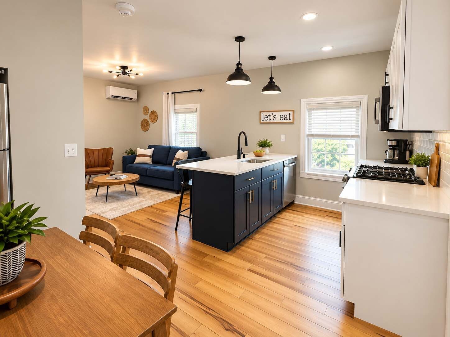 A modern kitchen with a central island, a dining area with a wooden table and chairs, and a living room with a sofa and a coffee table.