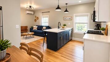 A modern kitchen with a central island, a dining area with a wooden table and chairs, and a living room with a sofa and a coffee table.