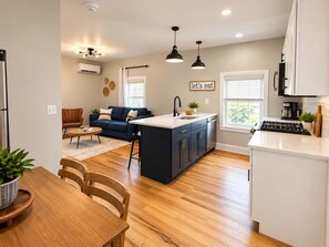 A modern kitchen with a central island, a dining area with a wooden table and chairs, and a living room with a sofa and a coffee table. - Jennifer's Elegant & Cozy Broadway Walkable Stay (Providence)