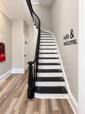 A staircase with a black handrail and white steps, a red fire alarm box, and a wall with 'hello & welcome.'