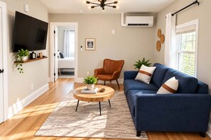 A living room with a blue sofa, a wooden coffee table, and a television mounted on the wall. - Jennifer's Elegant & Cozy Broadway Walkable Stay (Providence)