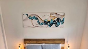 Un lit avec une tête de lit en bois, deux tables de chevet avec des lampes et une œuvre d’art abstraite accrochée au mur.