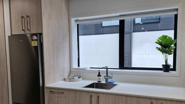 Une cuisine moderne avec des meubles en bois clair, un réfrigérateur en acier inoxydable, une fenêtre offrant une belle vue et un évier avec un robinet.