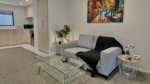 Una sala de estar moderna con una mesa de centro de vidrio, un sofá gris y un cuadro en la pared.