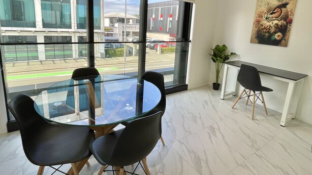 Una habitación moderna con una mesa y sillas de vidrio, un escritorio blanco y un ventanal con vistas a la calle.
