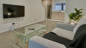 Una sala de estar moderna con una mesa de centro de vidrio, un televisor de pantalla plana, un sofá y una cocina al fondo.
