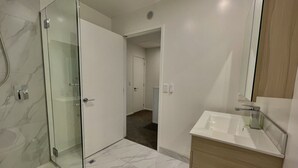 Un baño moderno con cabina de ducha de vidrio, un lavamanos blanco y un mueble de tocador de madera.