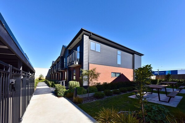 A modern building with a flat roof, a covered walkway, and a well-maintained garden with benches.