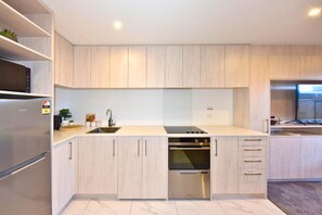 A modern kitchen with light wood cabinetry, stainless steel appliances, and a built-in oven.