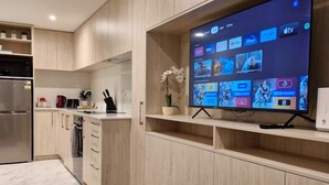 Cocina moderna con armarios de madera, horno integrado y un televisor de pantalla plana grande montado en la pared, mostrando varios servicios de transmisión.