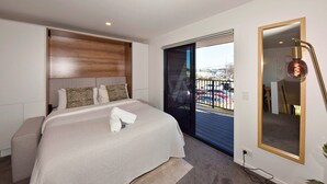 A hotel room with a bed, a bedside table, a large mirror, and a view of a parking lot through a sliding door. - Cosy CBD Studio Apartment 12 (Christchurch)
