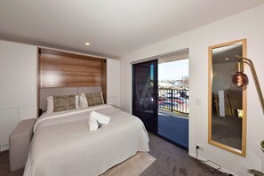 A hotel room with a bed, a bedside table, a large mirror, and a view of a parking lot through a sliding door.