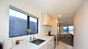 A modern kitchen with a large window, a sink, and a dining area with a table and chairs. - Cosy CBD Studio Apartment 12 (Christchurch)