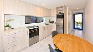 A modern kitchen with a built-in oven, a stainless steel refrigerator, and a dining area with a wooden table.