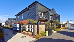 A modern two-story residential building with a balcony, a gated entrance, and a clear sky.