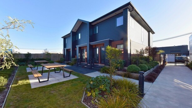 A two-story house with a patio, a small garden, and a gated driveway.