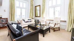 A living room with a black leather sofa, a white armchair, a coffee table, and a bookshelf.