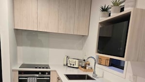 Una cucina moderna con mobili in legno chiaro, forno in acciaio inossidabile, microonde integrato, piano di lavoro bianco e un piccolo lavandino.