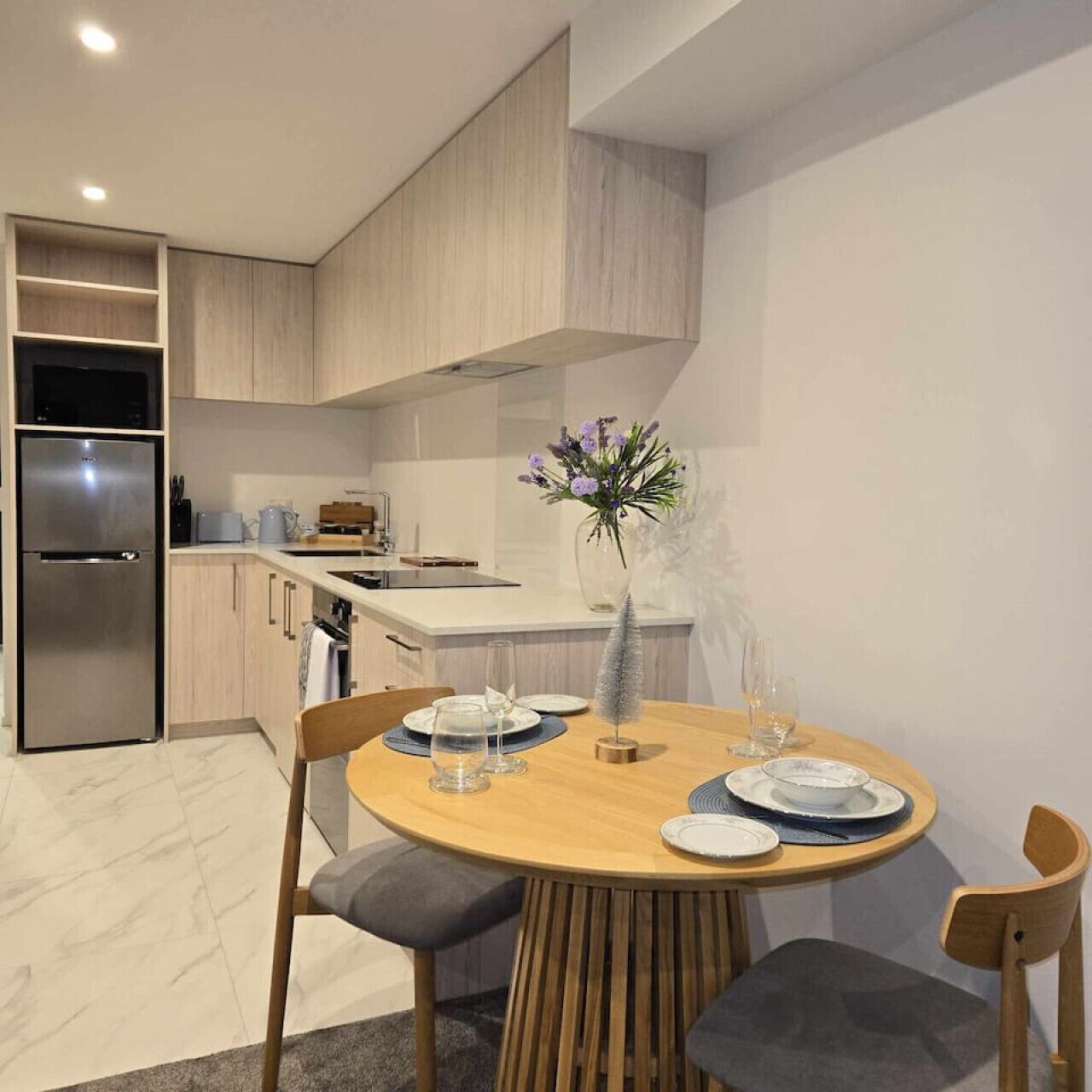 A modern kitchen with built-in appliances, a dining area with a round table, and a vase of flowers.