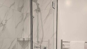 Une douche fermée par des parois en verre, dotée d’un pommeau de douche à main et d’un panneau de commande fixé au mur.