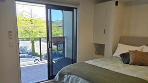 Une chambre comprenant un lit, une table de chevet, une fenêtre donnant sur un parking et une porte-fenêtre coulissante qui mène à un espace extérieur.