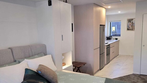 Une chambre avec un lit, une petite table et, au fond, un coin cuisine.