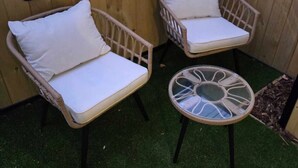 Deux fauteuils en osier avec des coussins blancs et une petite table ronde avec un plateau en verre.