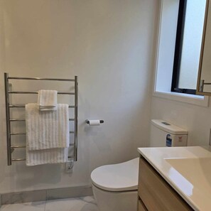 A bathroom with a toilet, a towel rack with towels, a toilet paper holder, and a window.