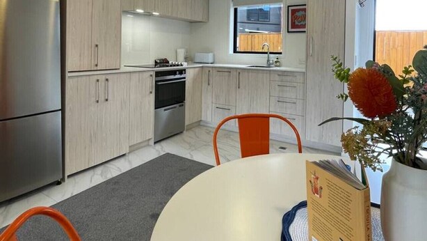 Eine moderne Küche mit hellen Holzschränken, Edelstahlgeräten und einem Essbereich mit weißem Tisch und orangefarbenen Stühlen.