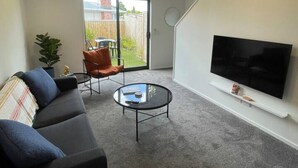 Ein modernes Wohnzimmer mit einer Couch, einem Couchtisch, einem Fernseher und einer Glasschiebetür, die zu einem Hinterhof führt.