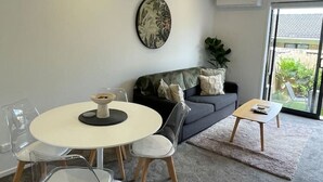 A modern living room with a round dining table, clear chairs, a grey sofa, and a small coffee table.