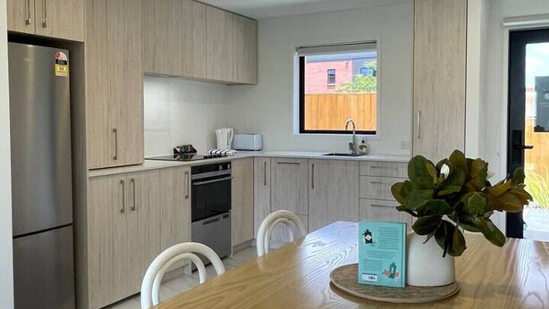 Une cuisine moderne avec des meubles de couleur bois clair, des appareils en acier inoxydable et une table à manger en bois assortie de chaises.