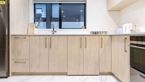 A modern kitchen with light wood cabinets, a stainless steel refrigerator, a built-in oven, and a window above the sink. - 10 Salisbury Cosy 2-Bed Retreat (Christchurch)